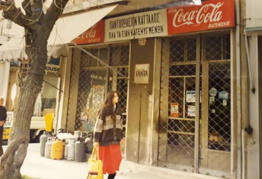 Фасад продуктового магазина с вывесками Coca‑Cola и прохожей у входа