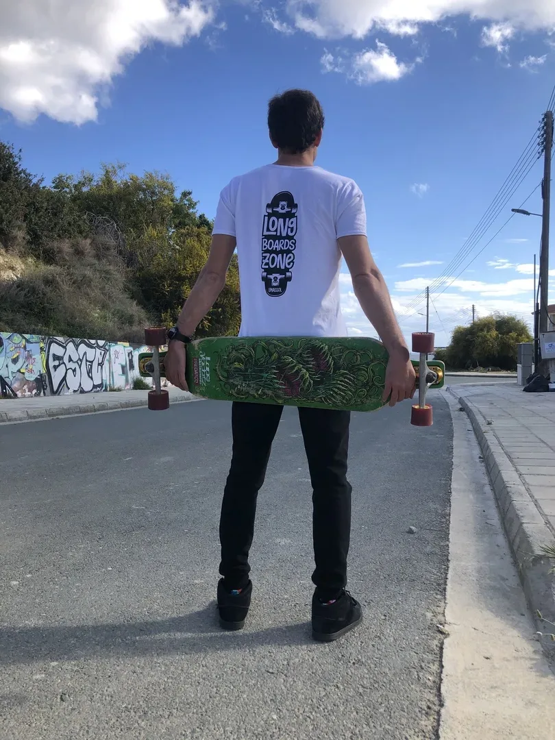 Райдер стоит спиной с зелёным лонгбордом и надписью Long Boards Zone на футболке Райдер стоит спиной с зелёным лонгбордом и надписью Long Boards Zone на футболке