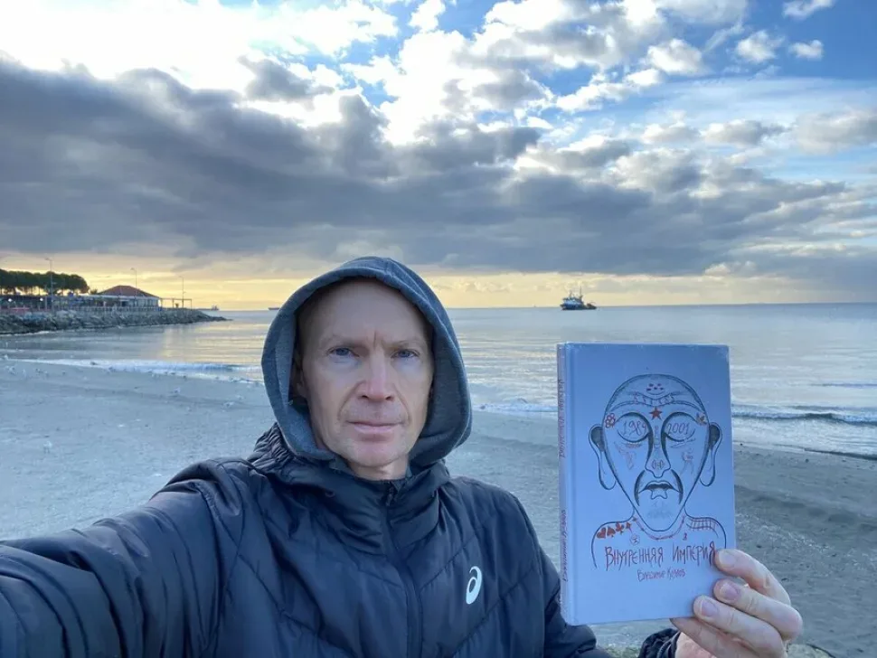 Писатель на пляже держит книгу «Внутренняя империя» на фоне моря