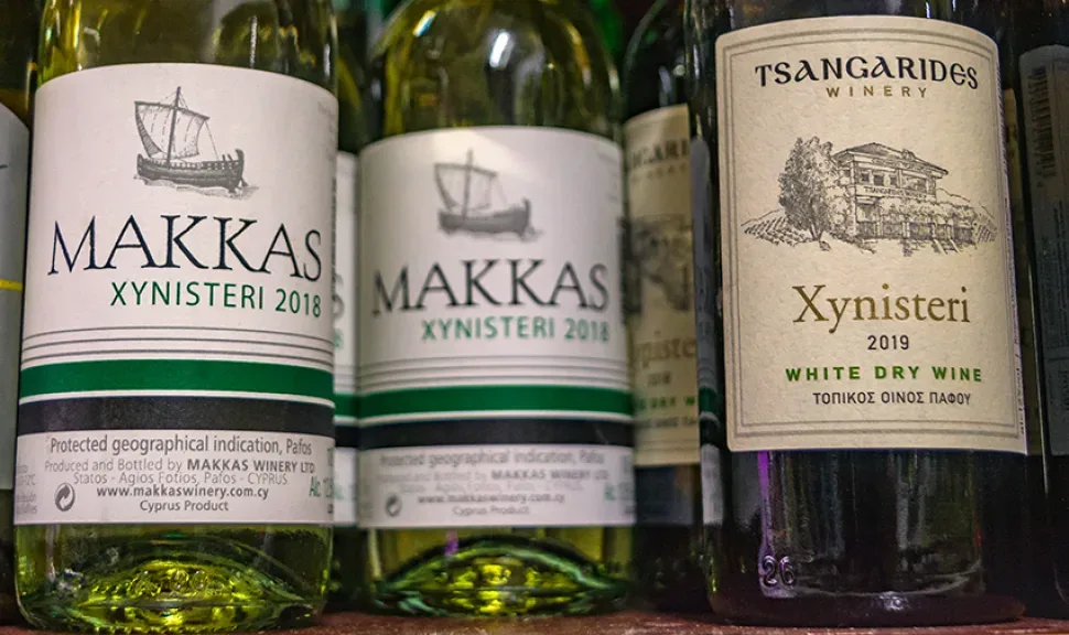 Ряд бутылок Makkas и Tsangarides Xynisteri на прилавке магазина