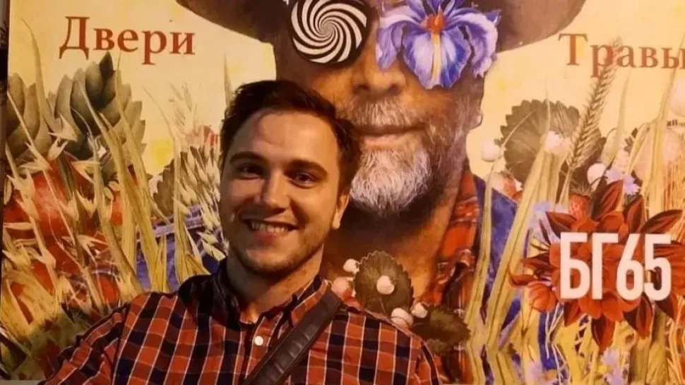 Андрей Чепелев на фоне афиши концерта Бориса Гребенщикова с надписью БГ65