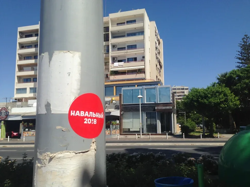 Светлая опора с круглой красной наклейкой кампании «НАВАЛЬНЫЙ 20!8» на фоне зданий