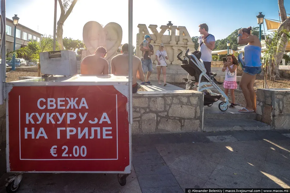 Куча людей у скульптуры и вывески с ценой за кукурузу на гриле