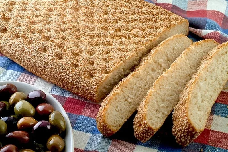 Лепёшка лагана с кунжутной посыпкой и миска разноцветных оливок