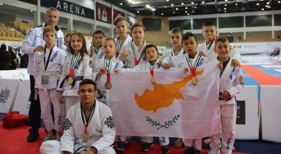 Дети‑спортсмены позируют с медалями и флагом Кипра на арене