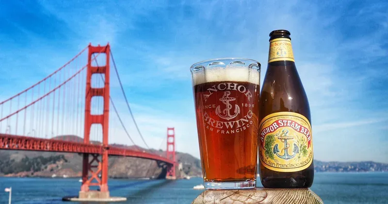 Стакан и бутылка на фоне пивного бара с надписью Anchor Brewing