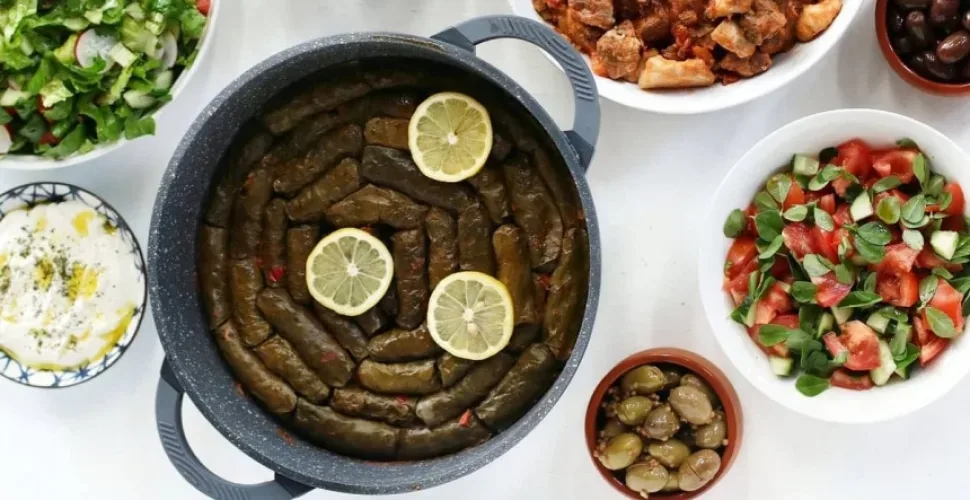 Кастрюля с купепьями, ломтики лимона и греческий салат с оливками