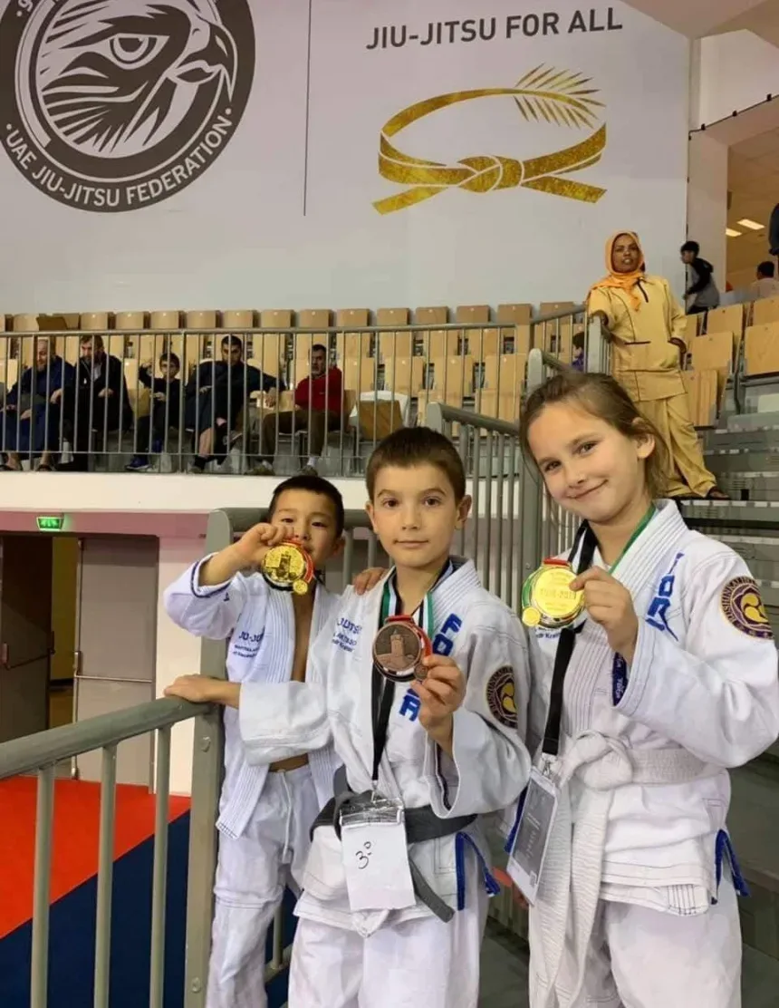 Три ребёнка‑призёра показывают медали на трибуне во время чемпионата