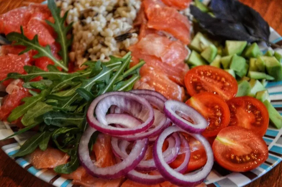 Тарелка с посыпанными кунжутом томатами, луком, руколой и лососем