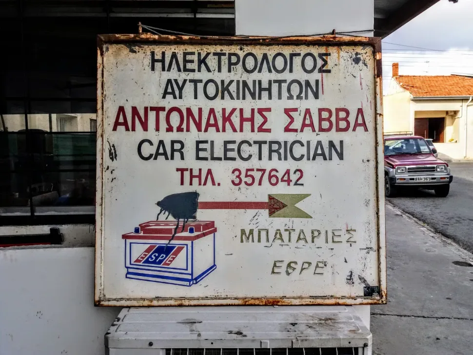 Ржавый старый металлический рекламный щит с надписью Car Electrician на греческом
