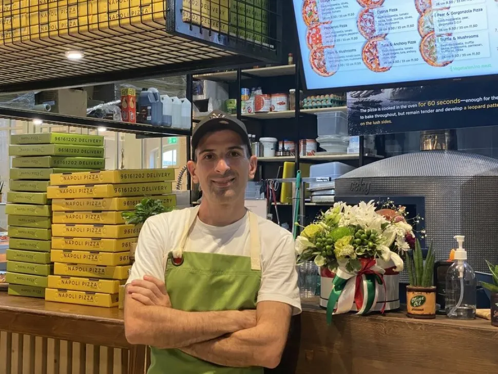 Сотрудник у стойки МО Pizza на фоне стопки коробок для доставки и цветов
