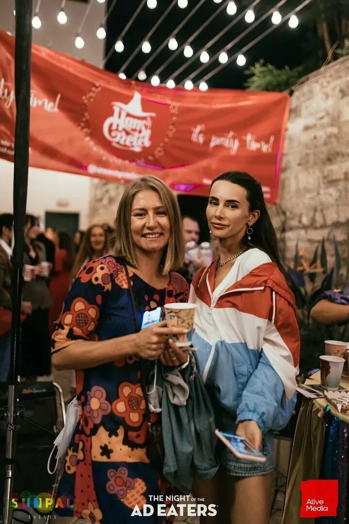 Две женщины держат чашки и позируют на фоне баннера организатора
