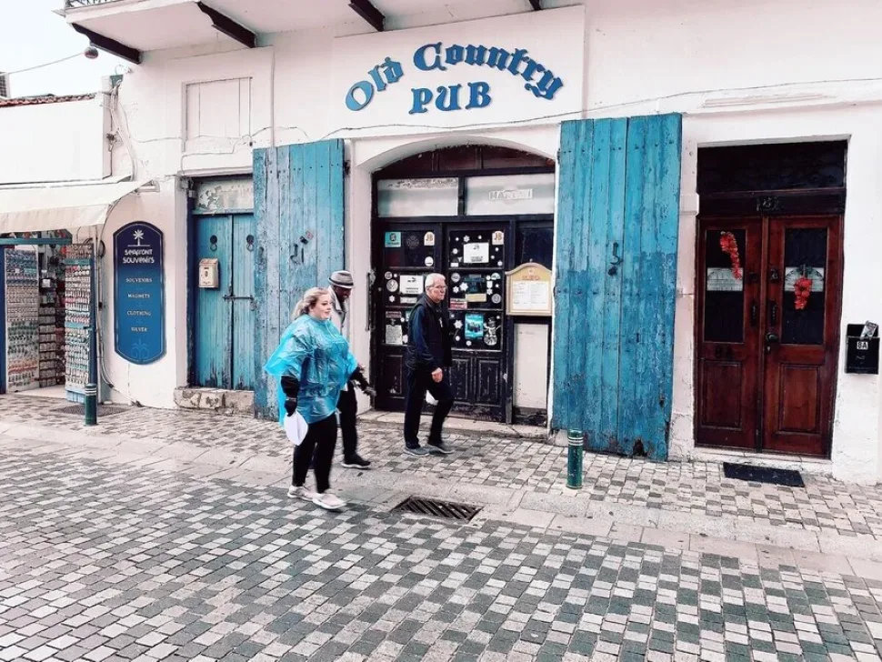 Фасад паба Old Country Pub с голубыми ставнями и прохожими