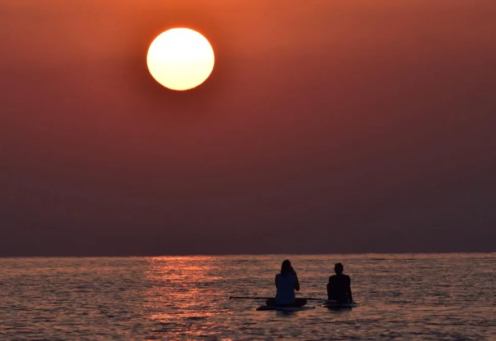 Несколько людей на SUP-досках плывут по морю при закате солнца