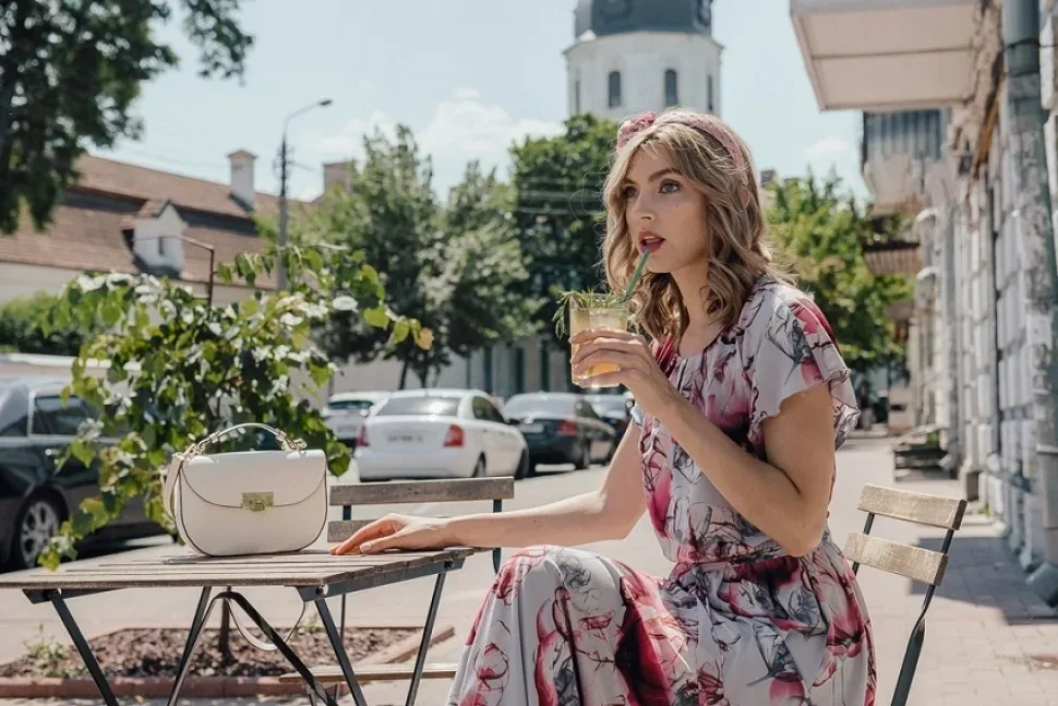 Женщина в летнем платье пьёт напиток за уличным столиком у церкви