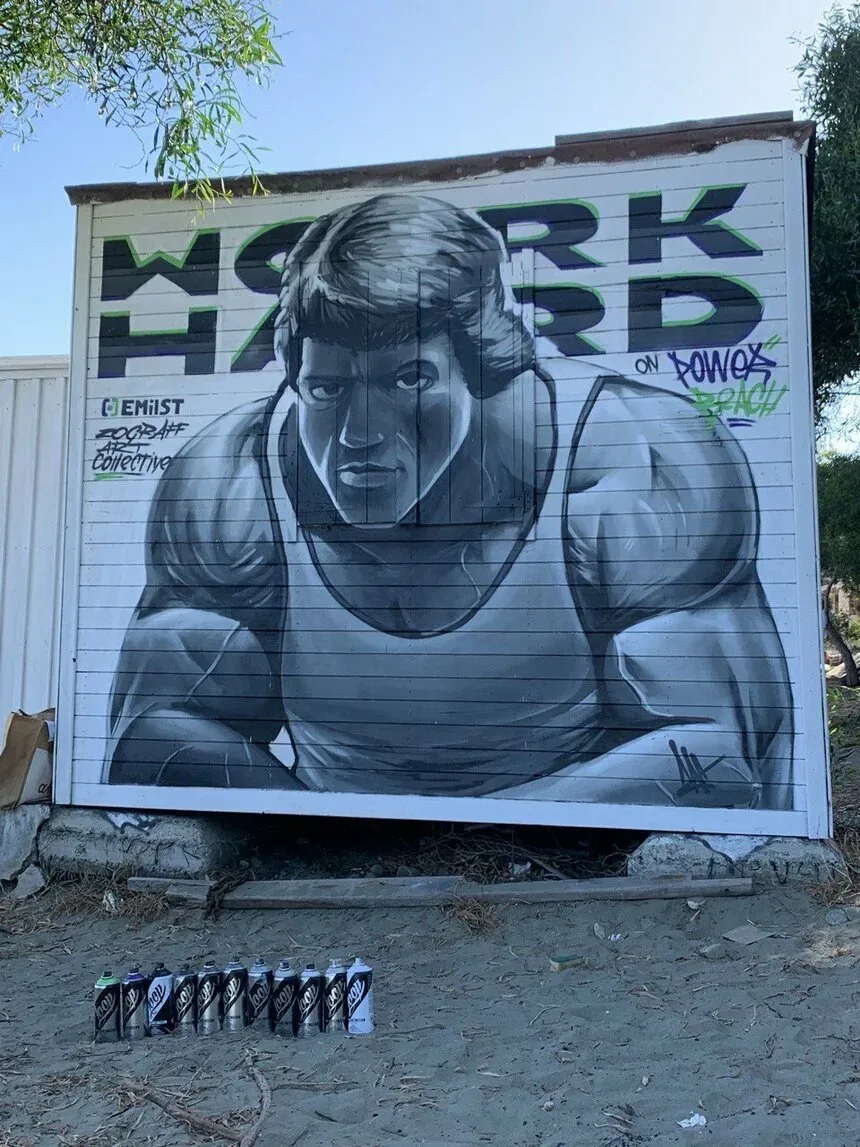 Граффити с мускулистым атлетом и надписью WORK HARD у пляжа