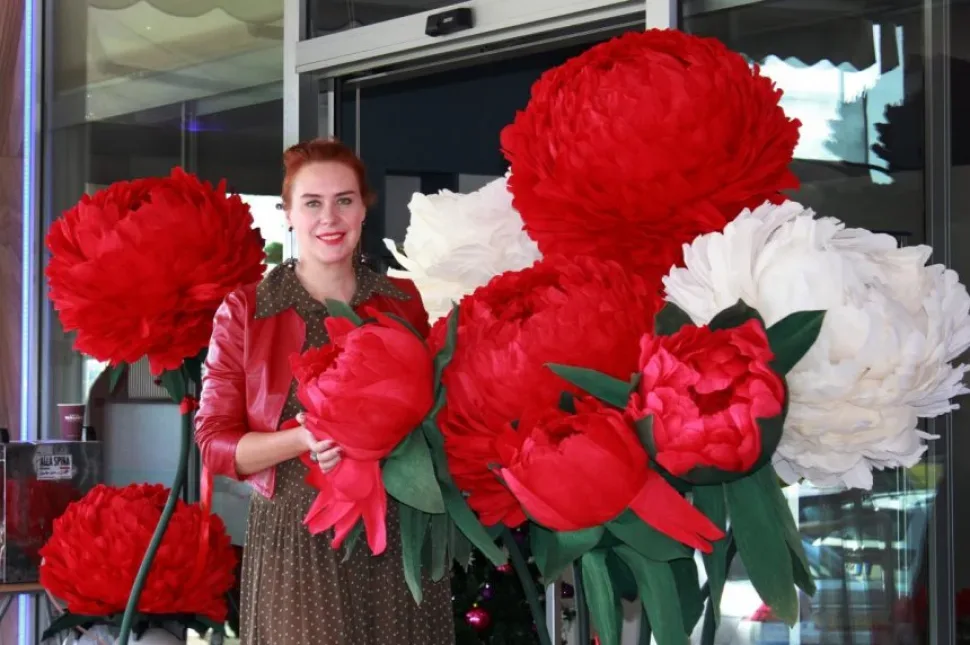 Женщина позирует рядом с большими декоративными красными цветами у входа