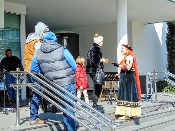 Женщина в традиционном костюме беседует с прохожими у сцены