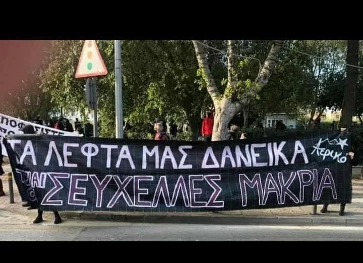Участники митинга держат черный баннер с греческой надписью антифа