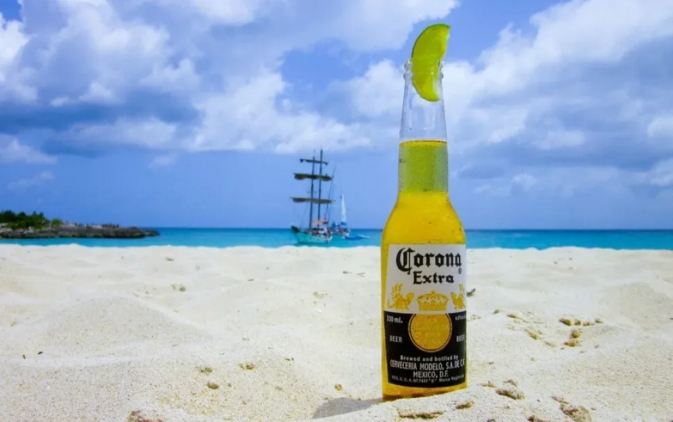 Бутылка пива Corona с долькой лайма, поставленная на песчаном пляже