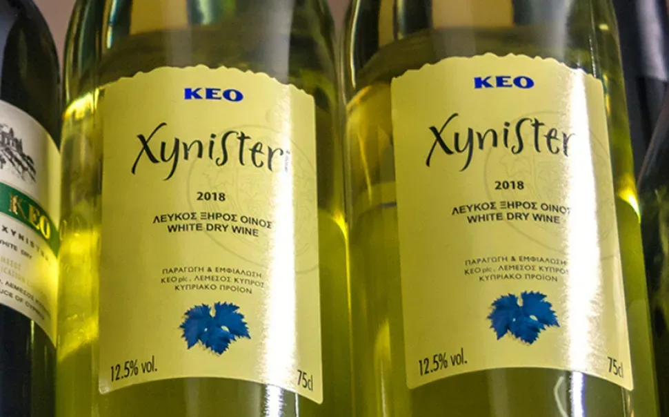 Двойной ряд бутылок KEO Xynisteri 2018 с жёлто-зелёными этикетками на полке