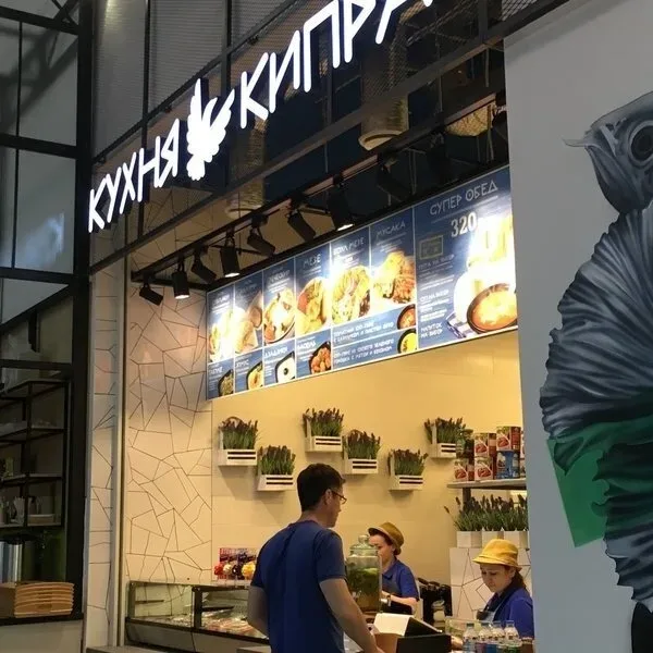 Интерьер и освещённая вывеска кафе сети Кухня Кипра в маркет‑формате