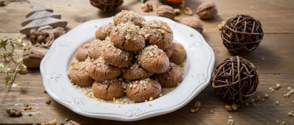 Горка тёплых меломакарона, посыпанных дроблёными грецкими орехами на белой тарелке