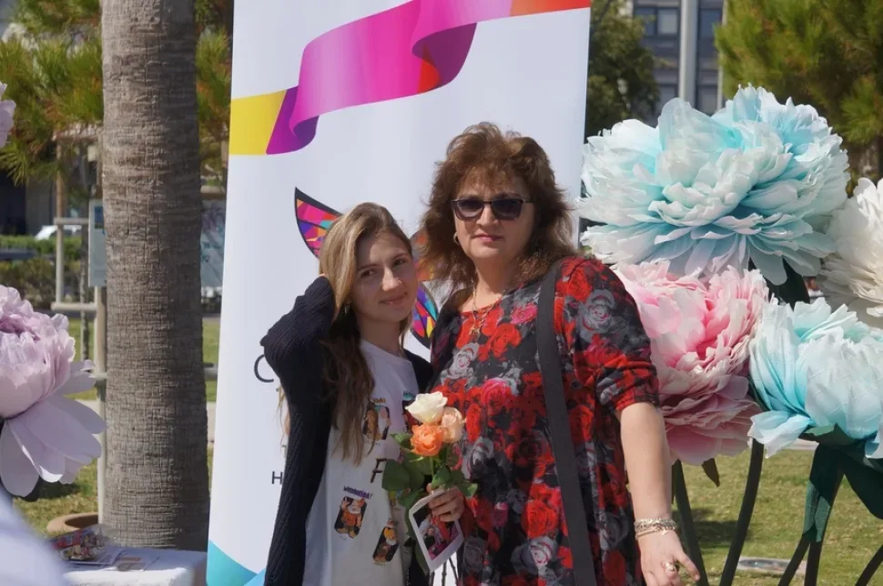 Мать и дочь позируют у баннера Cyprus Butterfly с вручённой розой