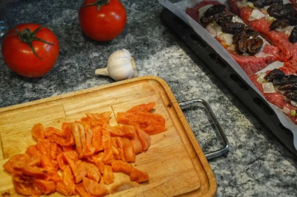 Нарезанная курага на доске и подготовленные отбивные на противне