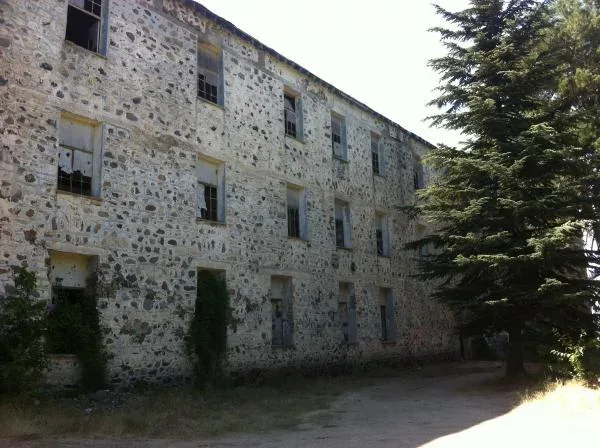Боковой фасад и каменные стены заброшенного отеля Беренгария среди деревьев