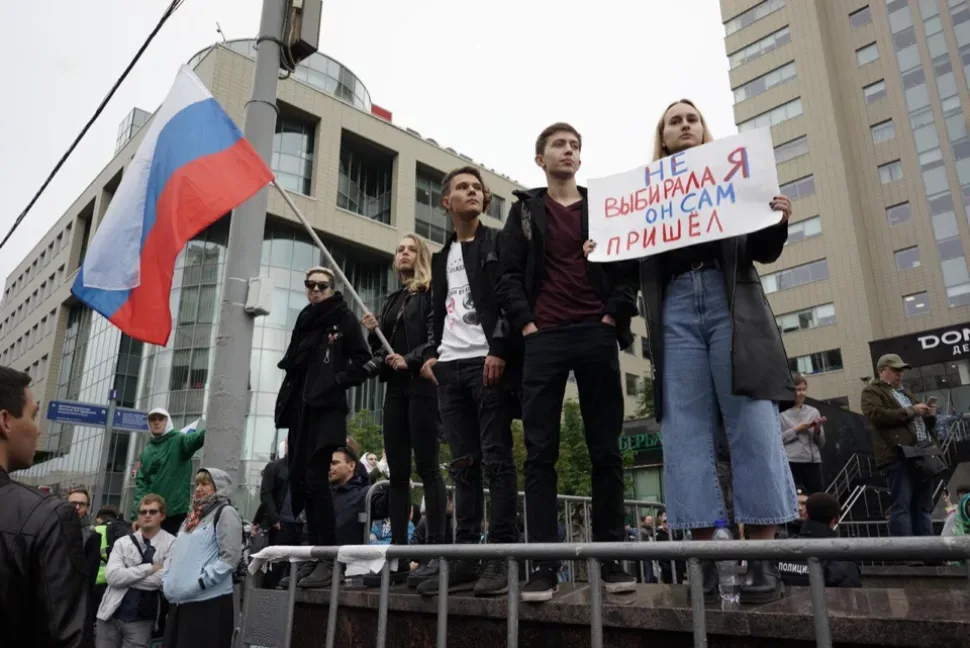 Молодые люди на возвышении с российским флагом и плакатом «Не выбирала я он сам пришел Молодые люди на возвышении с российским флагом и плакатом «Не выбирала я он сам пришел