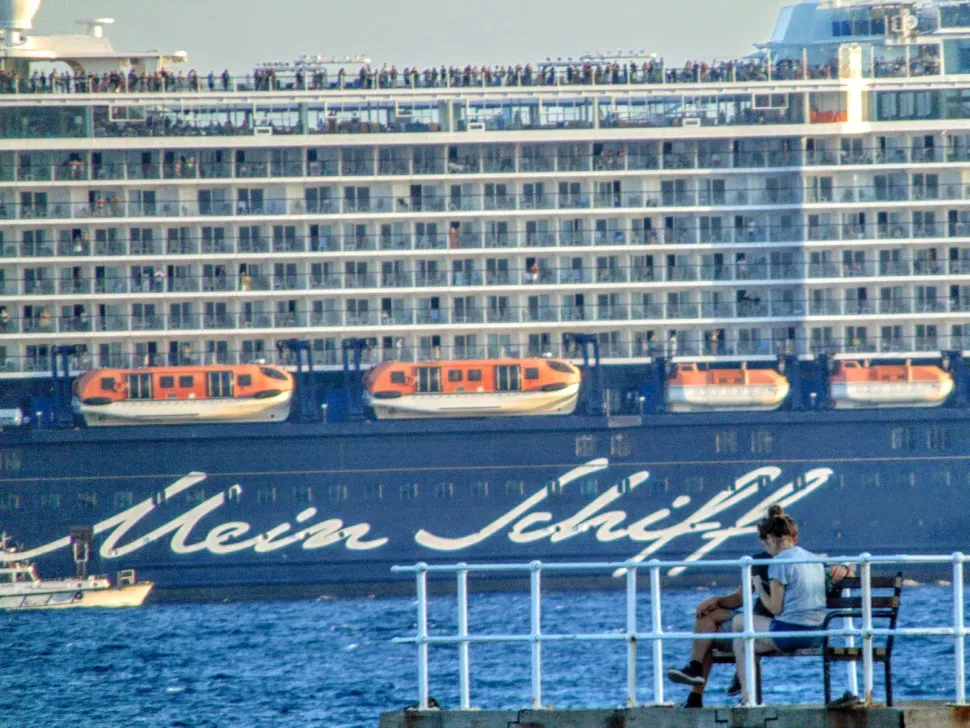 Крупный лайнер Mein Schiff у причала с людьми на верхней палубе и спасательными шлюпками Крупный лайнер Mein Schiff у причала с людьми на верхней палубе и спасательными шлюпками