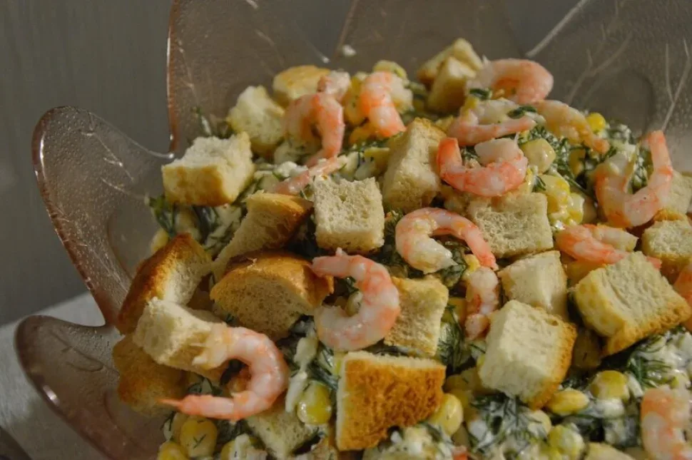 Сухарики насыпаны сверху салата из креветок и кукурузы