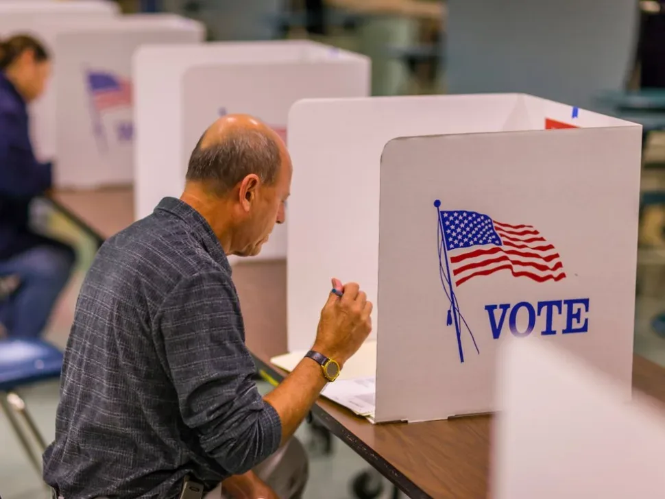 Избиратель в кабинке с американским флагом и надписью VOTE