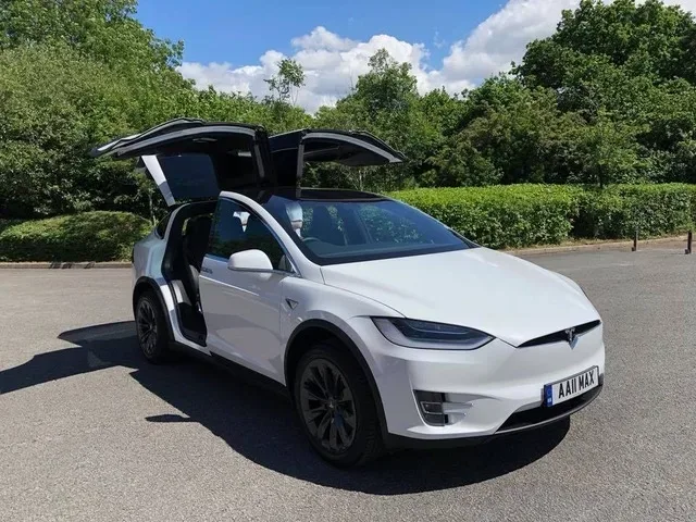 Белый Tesla Model X с распахнутыми распашными дверями на стоянке Белый Tesla Model X с распахнутыми распашными дверями на стоянке