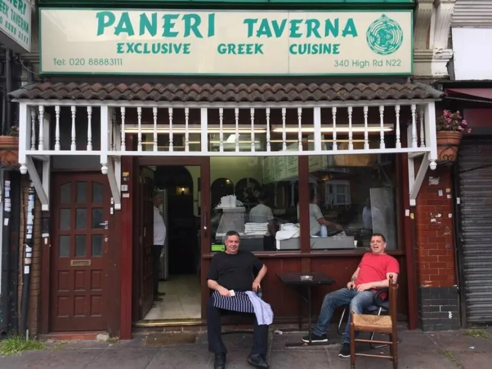 Вывеска Paneri Taverna в Вуд Грин и сидящие у входа люди