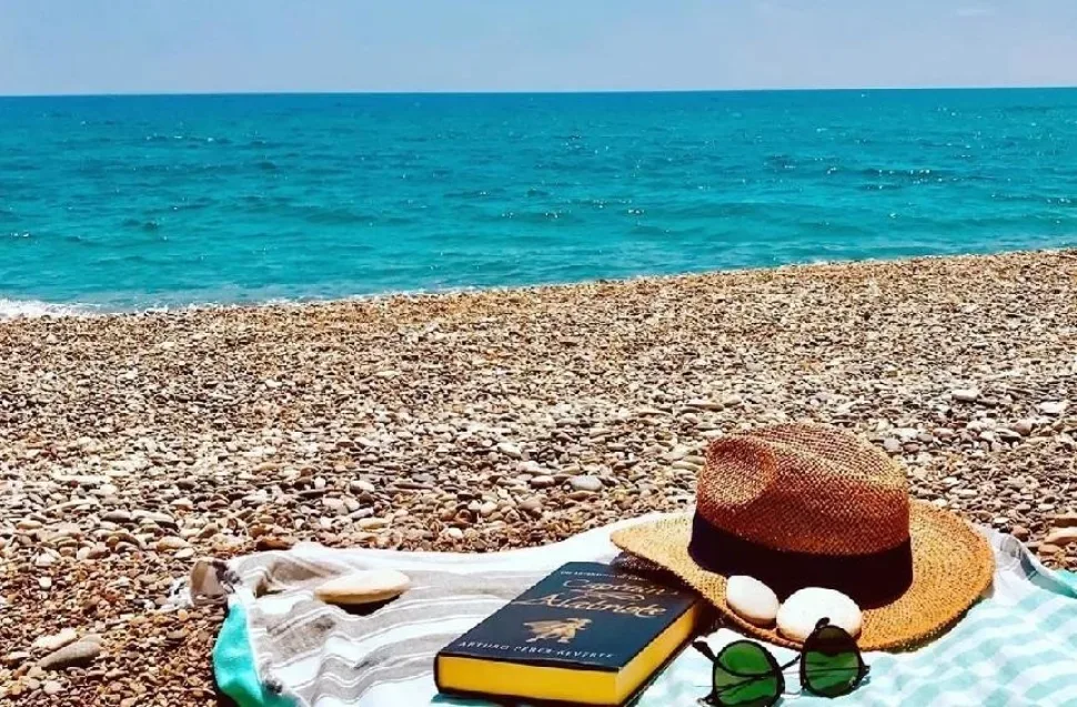 Отдых на гальке пляжа Авдиму с шляпой, очками и книгой