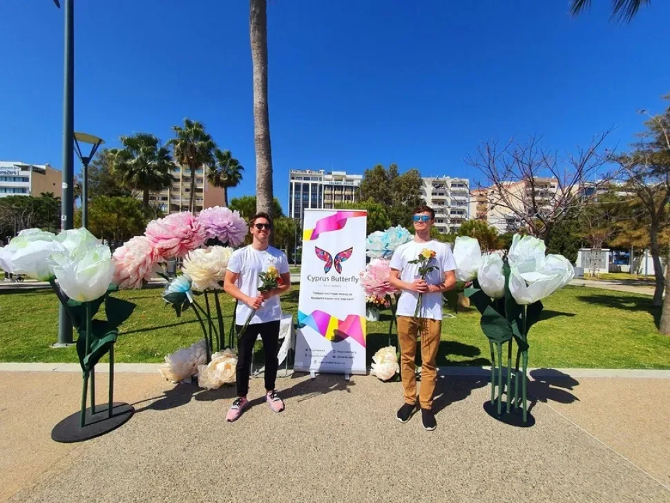 Два сотрудника Cyprus Butterfly стоят с розами у баннера на Молосе