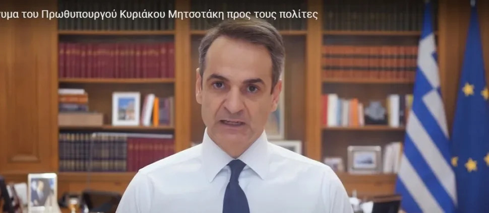 Кадр из видео YouTube: мужчина в кабинете на фоне книг и греческого флага Кадр из видео YouTube: мужчина в кабинете на фоне книг и греческого флага