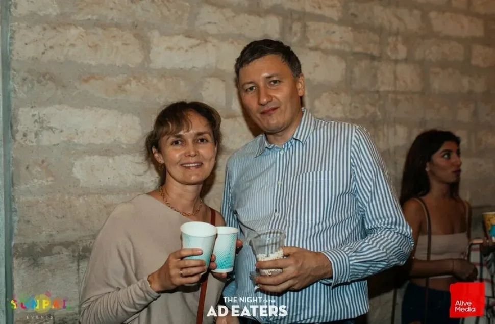 Пара гостей с бумажными стаканчиками на фоне каменной стены театра