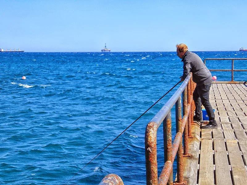 Мужчина с удочкой на ржавом пирсе смотрит на бурное море