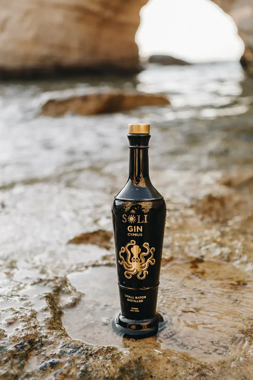 Черная бутылка Soli Premium Founders Edition Gin на морских камнях у воды