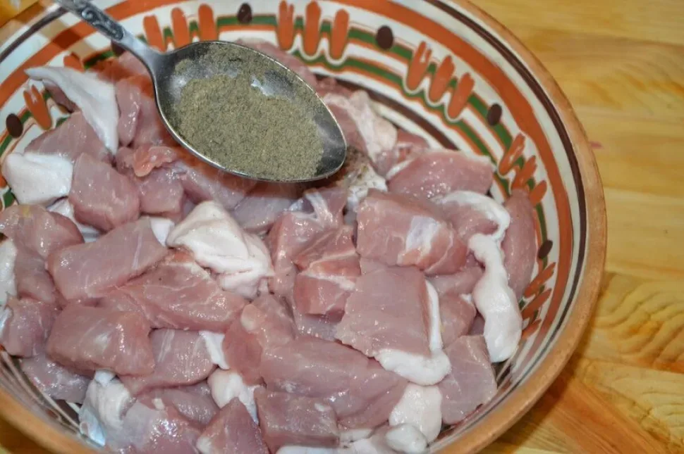 Кусочки свинины в миске посыпают молотым чёрным перцем