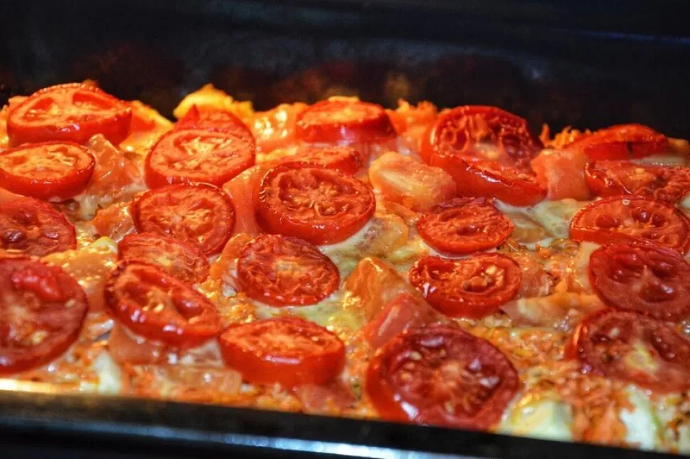 Противень с уложенными слоями мяса, овощей и сыром перед духовкой
