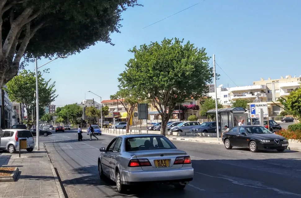 Улица на Кипре с припаркованными автомобилями и пешеходами на тротуаре Улица на Кипре с припаркованными автомобилями и пешеходами на тротуаре
