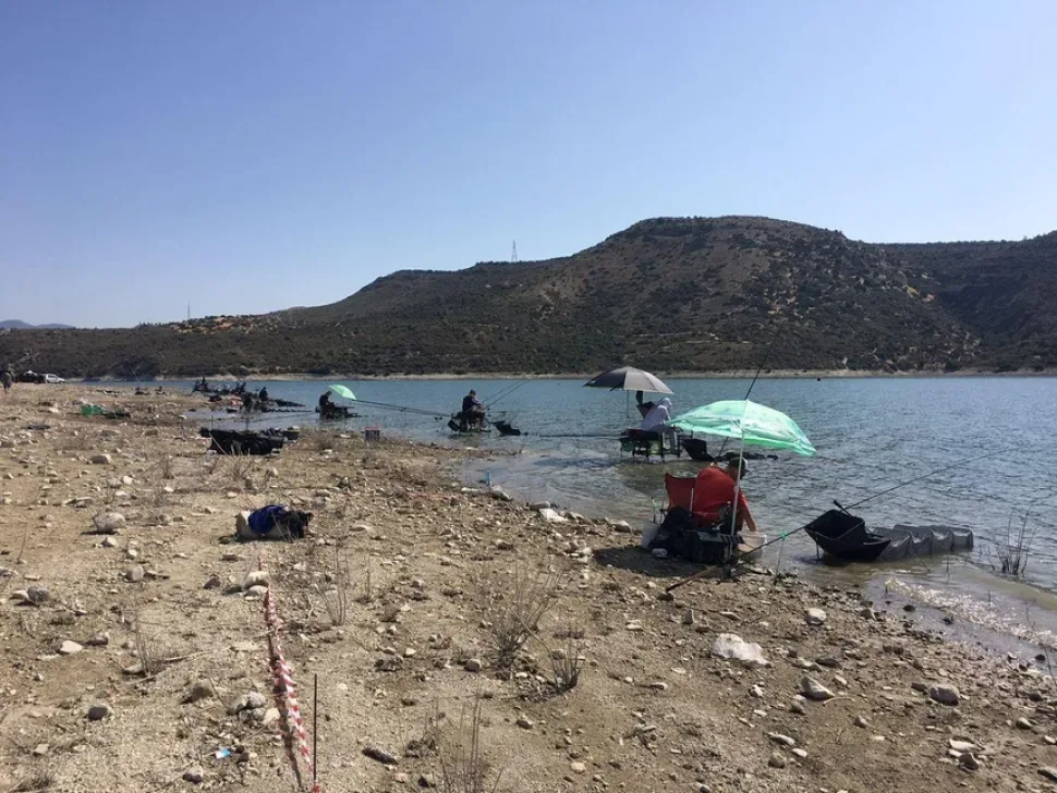 Ряд участников с зонтами и удилищами на дамбе Курис во время чемпионата