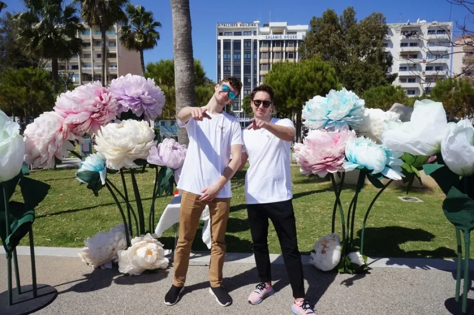 Два молодого сотрудника в футболках Cyprus Butterfly возле цветочной фотозоны