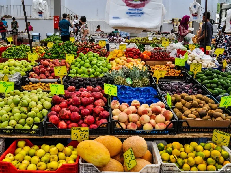 Рынок с лотками свежих фруктов и ценниками на местные продукты