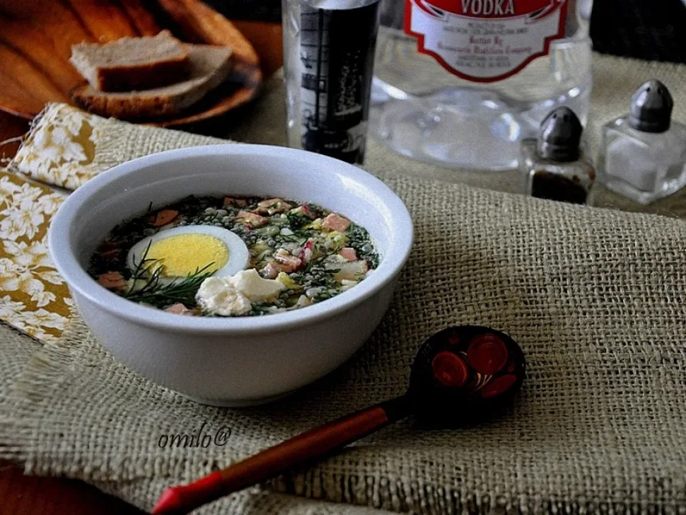 Окрошка в миске с половинкой яйца и бутылкой водки на фоне