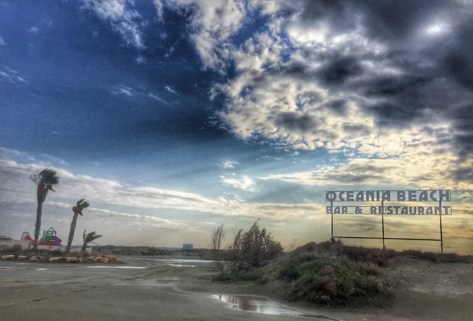 Пустой пляж с облачным небом и вывеской «Oceania Beach Bar & Restaurant